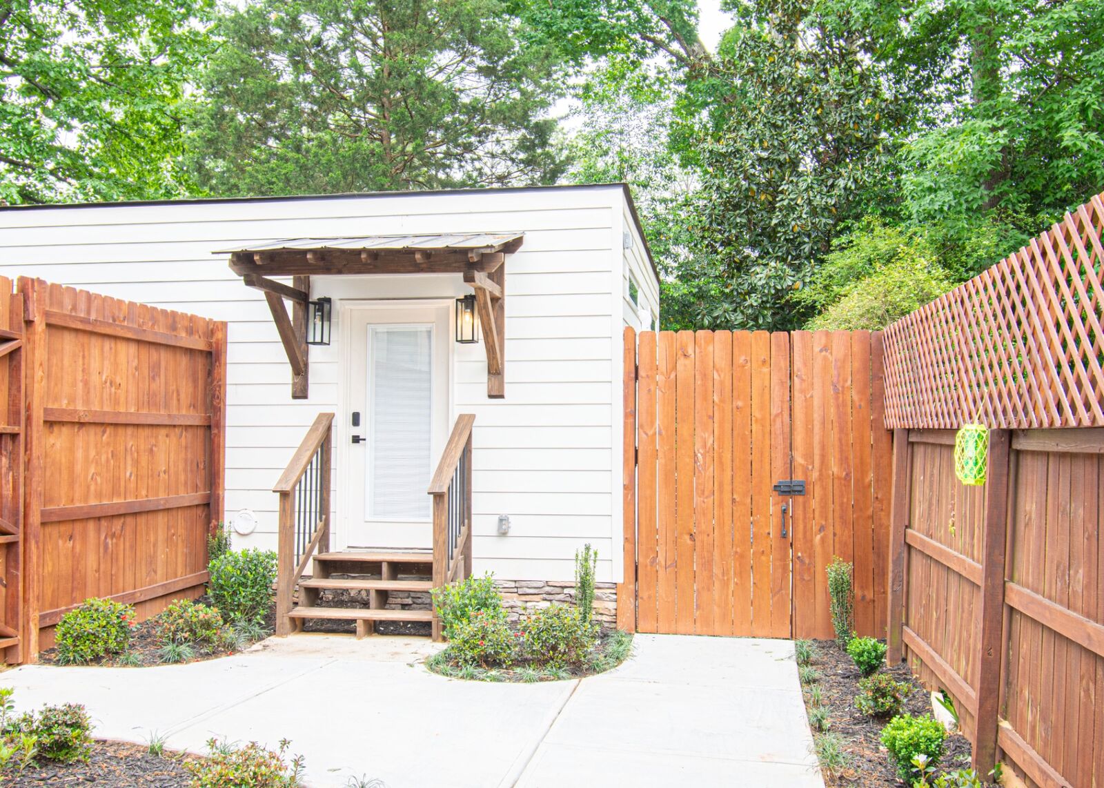 Completed ADU exterior with white siding, timber awning, and cedar privacy fence in Decatur